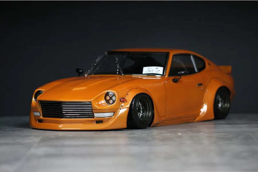 An orange painted RC drift car body styled as a classic Datsun Fairlady Z S30 with wide body fenders and deep dish wheels.