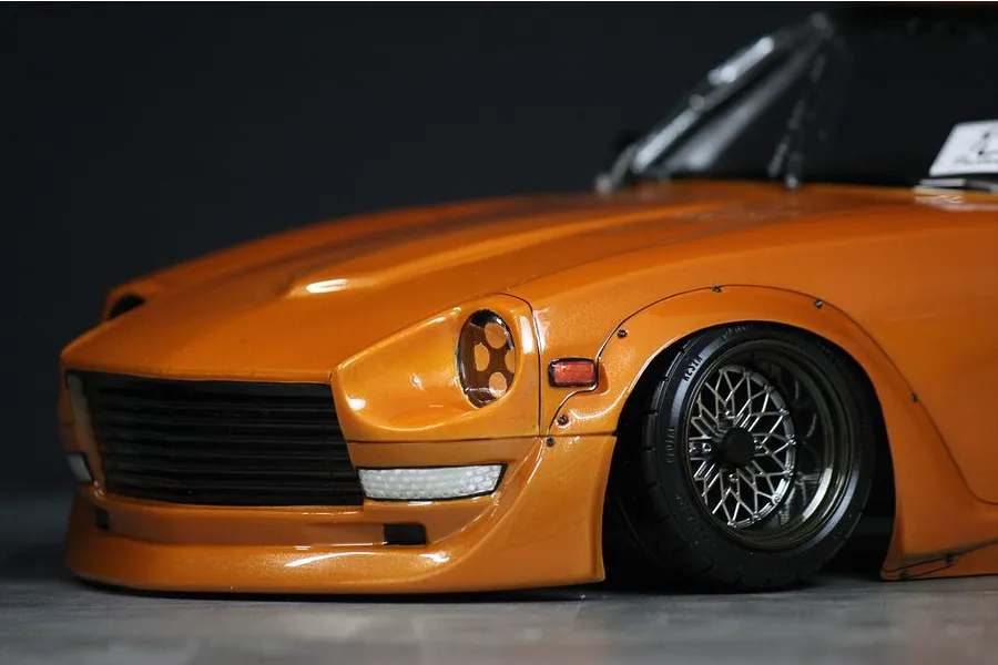 Close-up front quarter view of the orange Pandora RC S30 Fairlady Z body shell mounted on an RC chassis with mesh wheels.