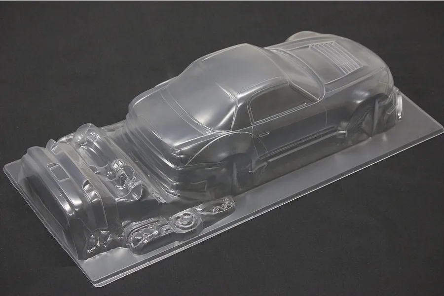 Unpainted clear polycarbonate RC car body shell with additional molded parts on a dark background.