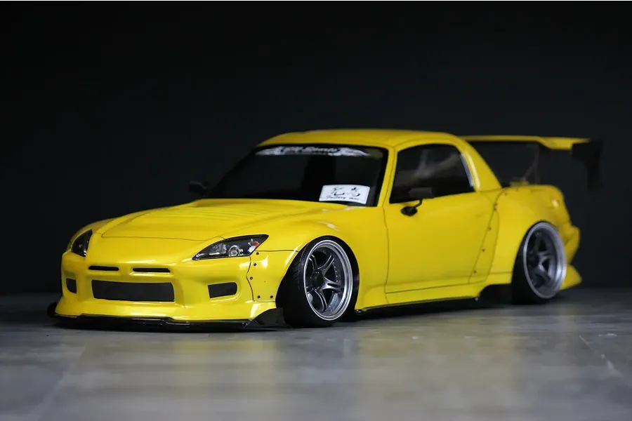 A painted yellow Honda S2000 RC drift car body shell with aftermarket wide body kit, rear wing, and custom wheels against a dark background.