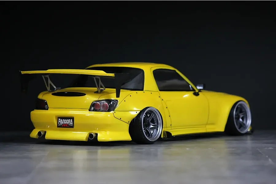 Rear three-quarter view of a yellow Honda S2000 RC drift car body with wide body fenders, large rear wing, and Pandora RC license plate against a dark background.