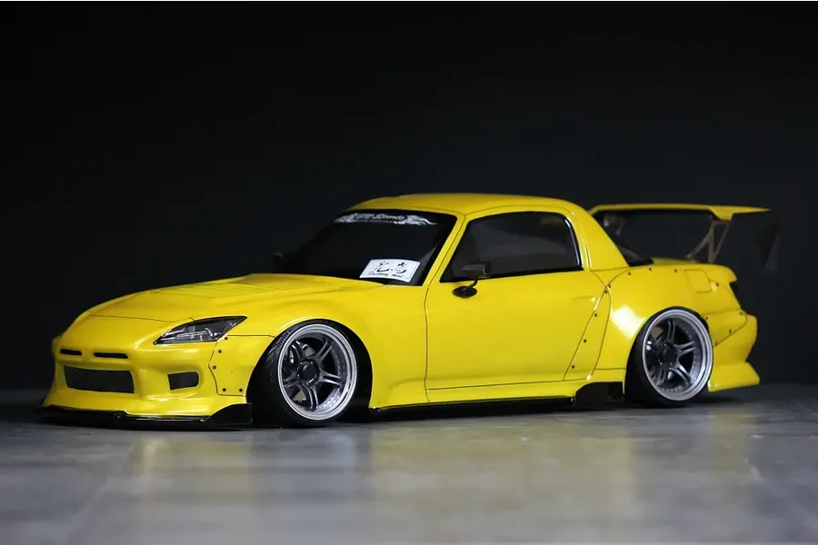 Painted yellow Honda S2000 RC drift car body with wide body kit and rear wing against a dark background.