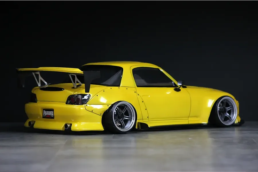Rear three-quarter view of a yellow Pandora RC Honda S2000 drift RC car body shell with a large rear wing and aftermarket wheels.