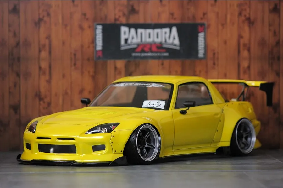 Yellow Honda S2000 RC drift car body shell with custom widebody kit and rear wing parked in front of a Pandora RC sign.