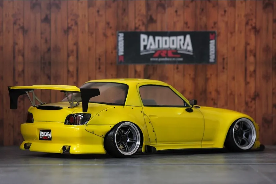 Custom painted yellow Honda S2000 RC drift car body shell with wide body kit and rear wing in front of a wood-pattern backdrop.