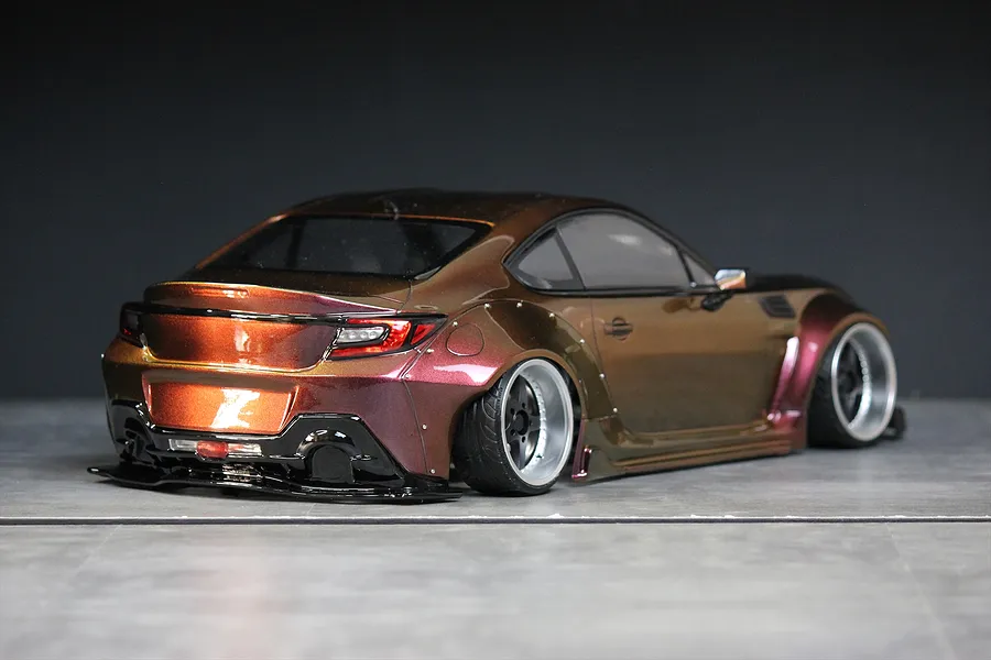 Rear three-quarter view of a custom painted RC drift car body styled as a Toyota GR86 with wide fenders and deep dish wheels.