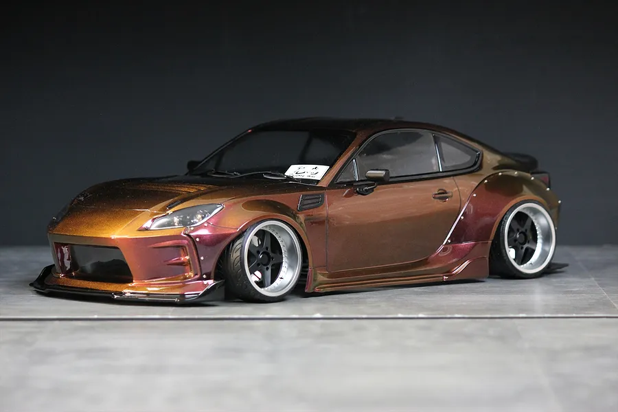 Custom painted RC drift car body shell mounted on a chassis with wide body kit and deep dish wheels against a dark background.