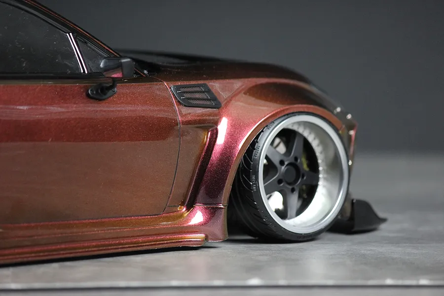 Close-up of a metallic bronze RC drift car body showing the front fender, wheel, and side mirror against a neutral background.