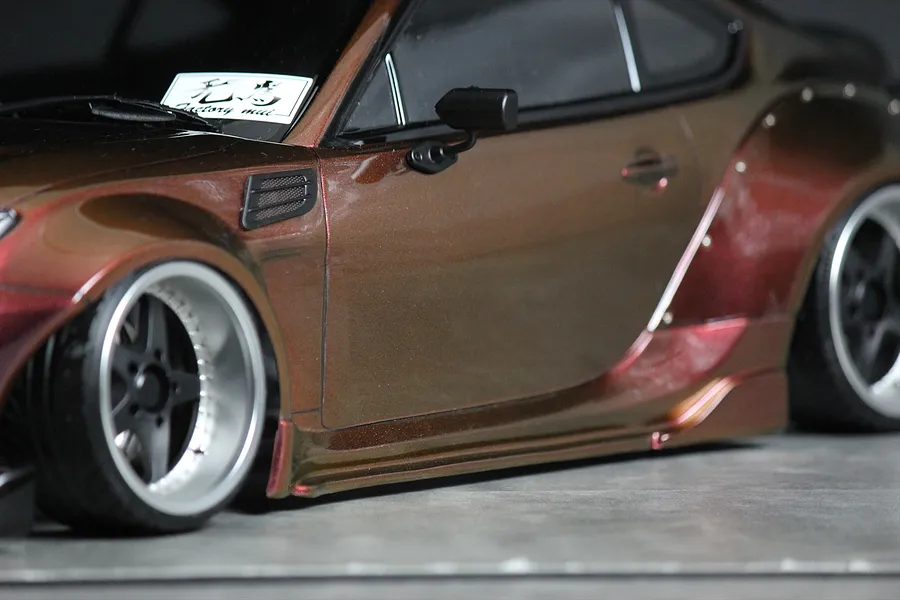 Close up side profile of a custom RC drift car body with brown metallic paint, wide fenders, and deep dish wheels.