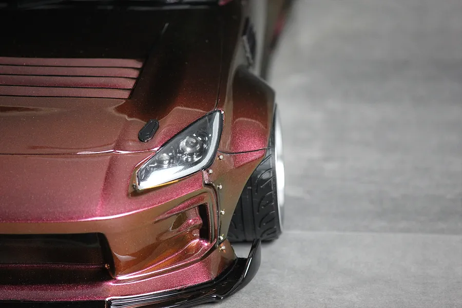 Close-up of the front corner of a metallic brown and red RC drift car body shell showing the headlight and wide fender.