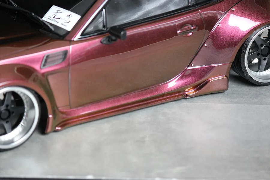 Close-up side view of a metallic burgundy RC drift car body showing wide fenders, side skirts, and wheels.