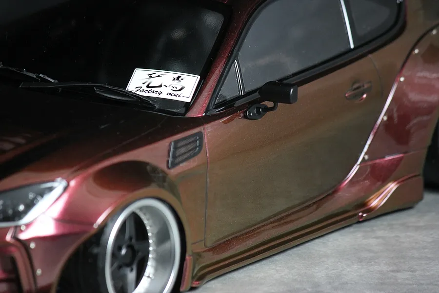 Close-up of the front side section of a metallic red RC drift car body showing the side mirror, fender, and wheel.