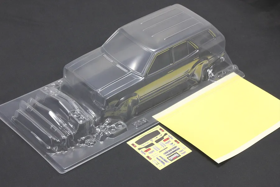 Unpainted clear polycarbonate RC car body shell with separate parts, decal sheet, and window mask on a dark background.