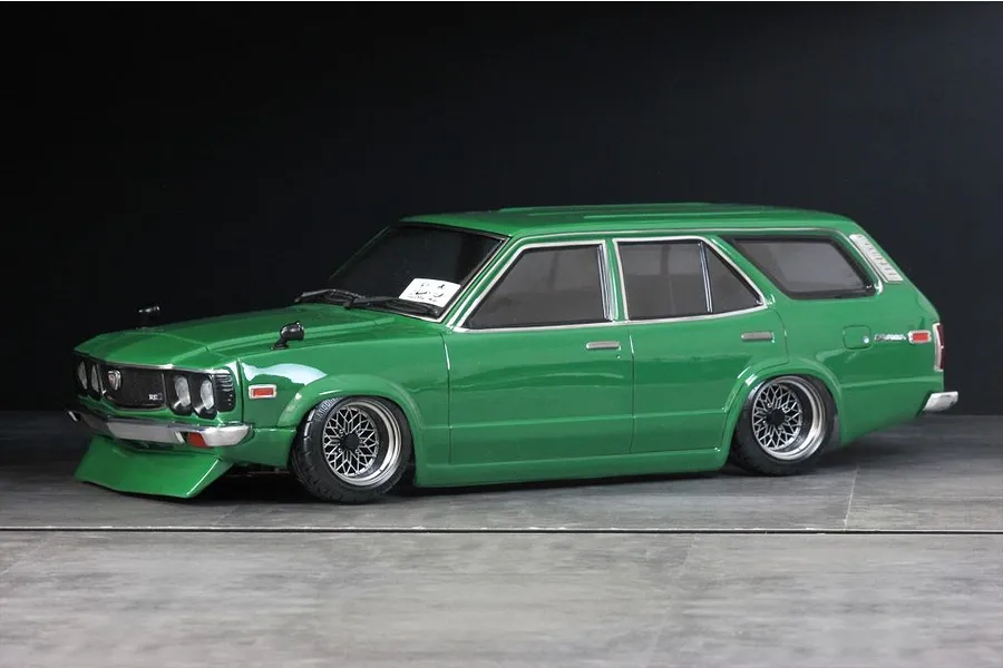 Green RC drift car body styled as a classic station wagon with custom wheels, parked on a grey studio floor against a dark background.