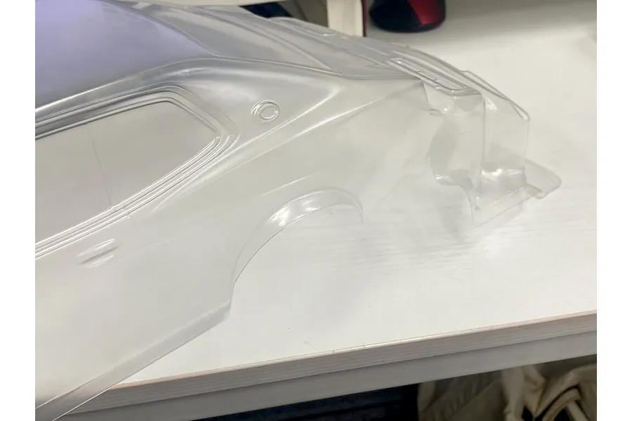 Unpainted clear polycarbonate RC car body shell resting on a white workbench surface.