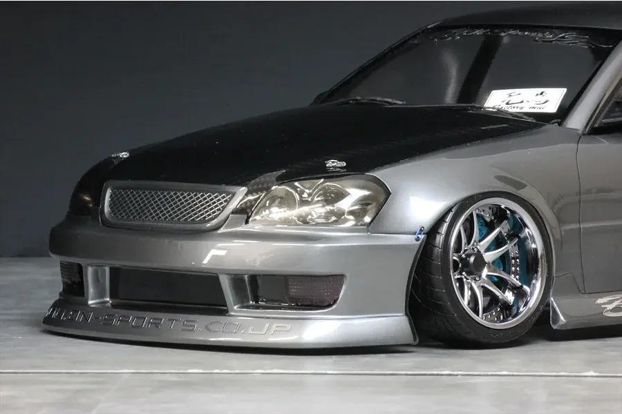 Close-up front quarter view of a grey RC drift car body with carbon hood, chrome wheels, and BN-Sports branding.
