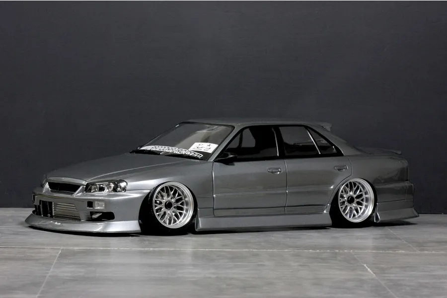 Side-profile view of a grey Pandora RC Nissan ER34 Skyline 4-door drift body shell fitted with custom silver mesh wheels.