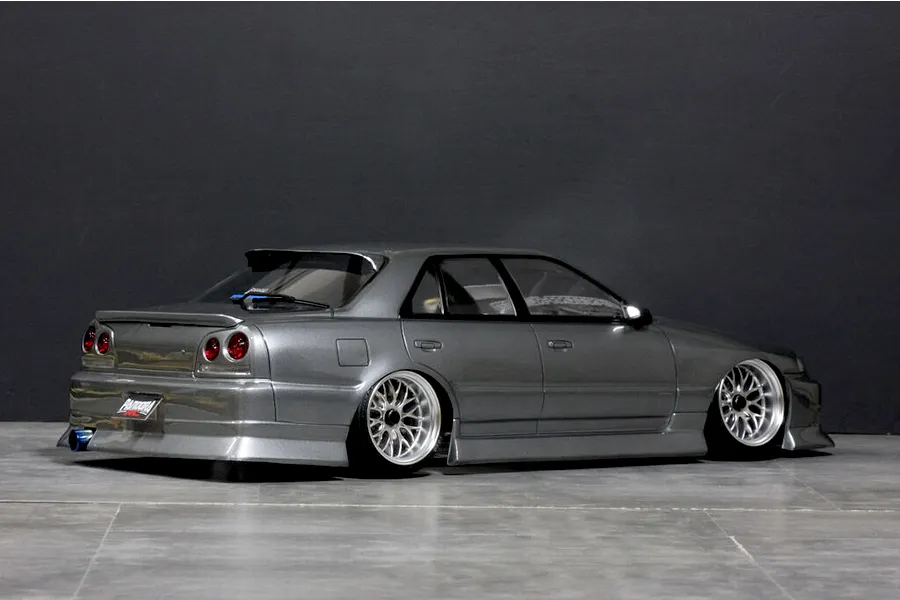 Rear three-quarter view of a painted grey Pandora RC ER34 Skyline 4-door drift body shell on a studio floor with dark background.