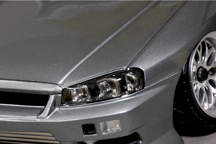 Close-up view of the front headlight and bumper section of a grey metallic RC car body shell.