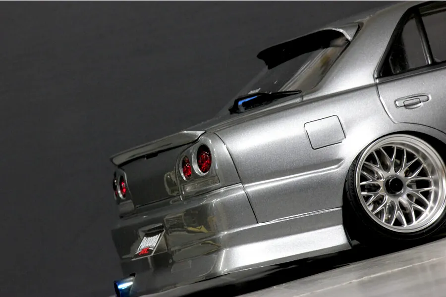 Close-up rear angle view of a silver Pandora RC ER34 Skyline 4-door drift car body shell showing tail lights, rear wheel, and exhaust.