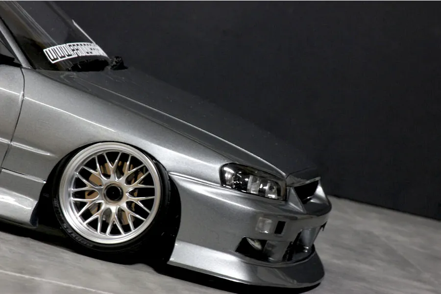Close-up front quarter view of a silver RC drift car body shell showing the front wheel, bumper, and headlights against a dark background.