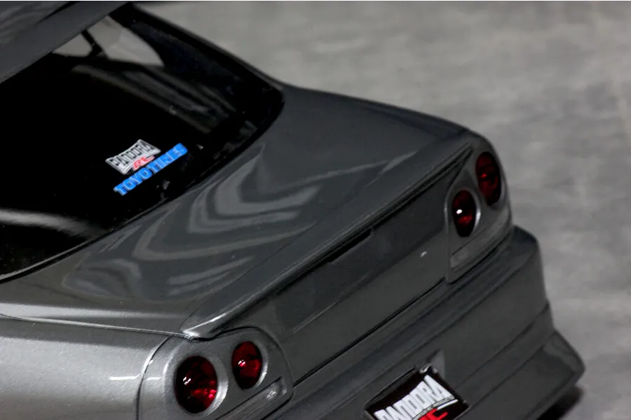 Close-up rear angle of a grey RC car body shell, showing trunk lid, rear lights, spoiler, and branded decals.