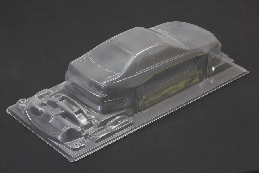 Unpainted clear polycarbonate 1/10 scale RC car body shell with separate parts tray on a dark surface.