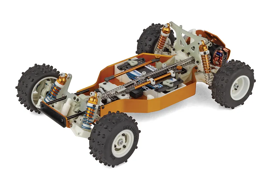 High angle studio shot of the Team Associated RC10 4WD RC buggy chassis showing the chain drive system, gold shocks, and knobby tires on white wheels.