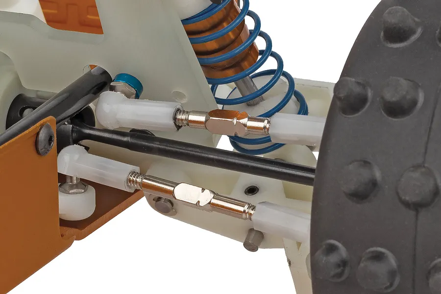 Close-up studio view of the RC car suspension, turnbuckles, and spiked rubber tyre against a plain white background.