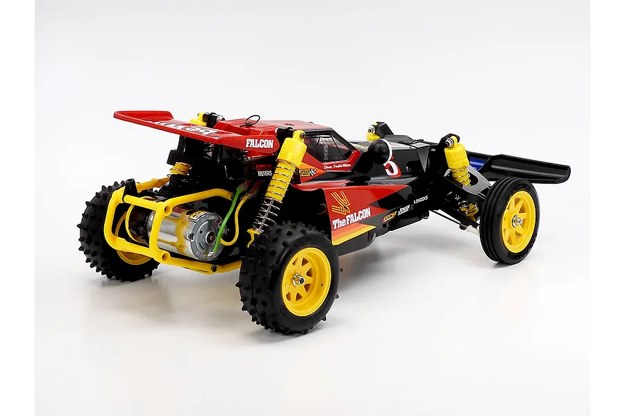 Rear-three-quarter studio view of the Tamiya The Falcon 2026 RC buggy, showing its red and black body, yellow wheels, and rear motor.