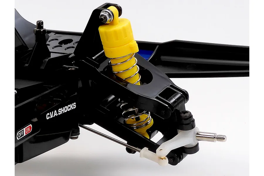 Close-up of front suspension on a Tamiya RC buggy showing a yellow C.V.A. shock absorber, black plastic arms, and metal steering linkage.