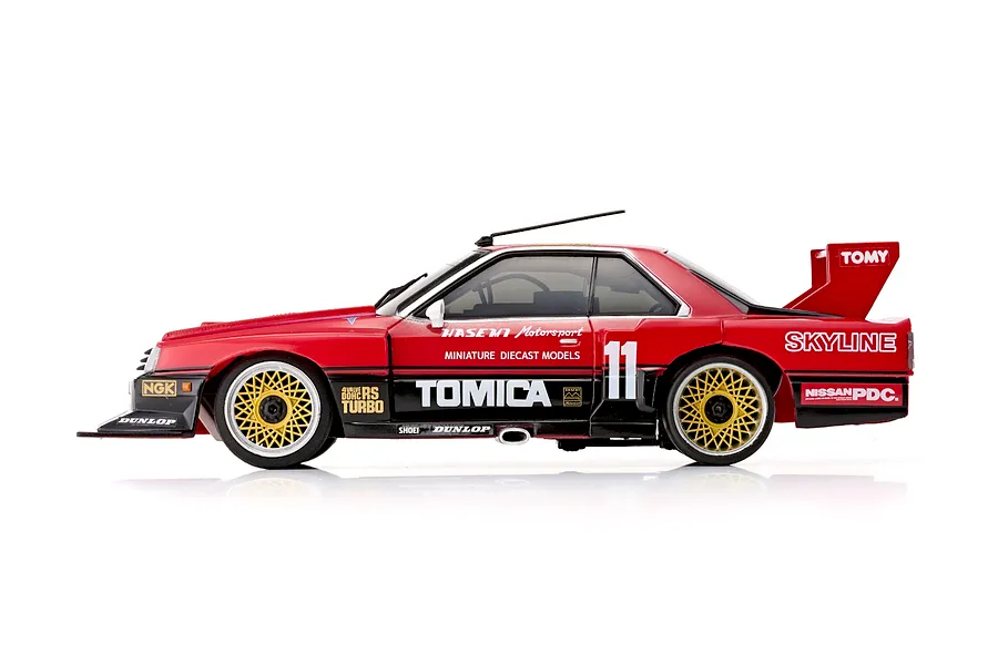 Side profile of the Kyosho First Mini-Z 1982 Nissan Super Silhouette RC car in red and black with gold mesh wheels and racing livery.