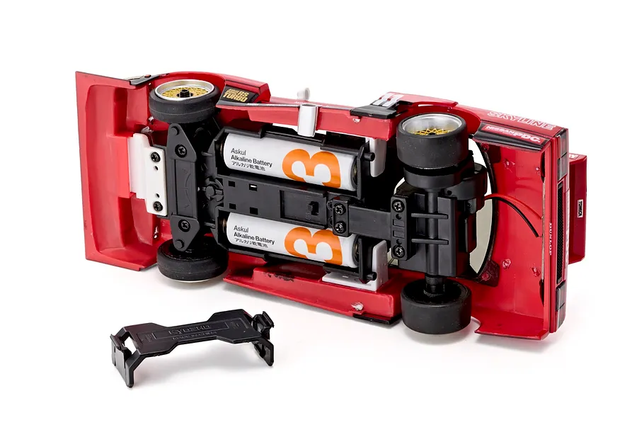 Underside view of the Kyosho First Mini-Z 1982 Nissan Super Silhouette RC car showing inserted batteries and battery cover.