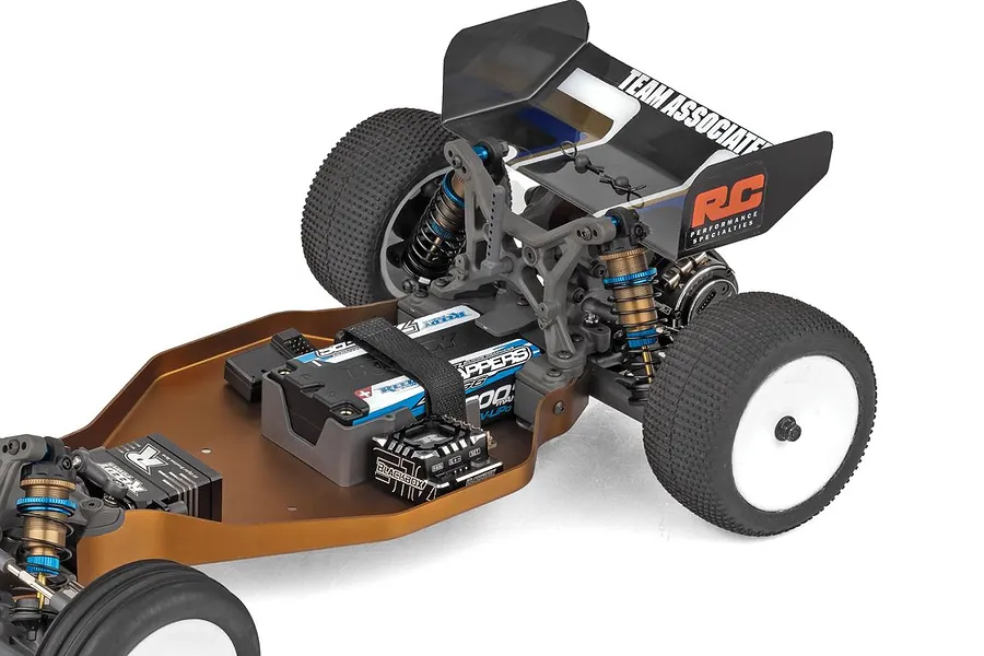 Close-up rear chassis view of the Team Associated RB10 showing the brown aluminum deck, rear suspension, battery, and wing against a white background.