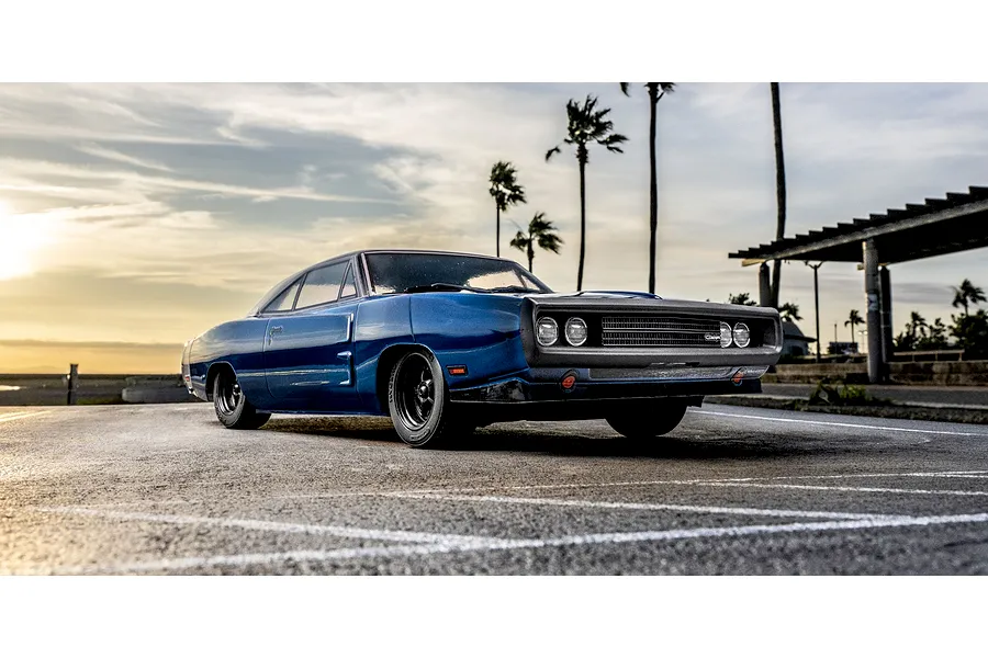 Kyosho Fazer MK2 1970 Dodge Charger Tuned blue RC car parked outdoors on paved ground with palm trees in the background during sunset.