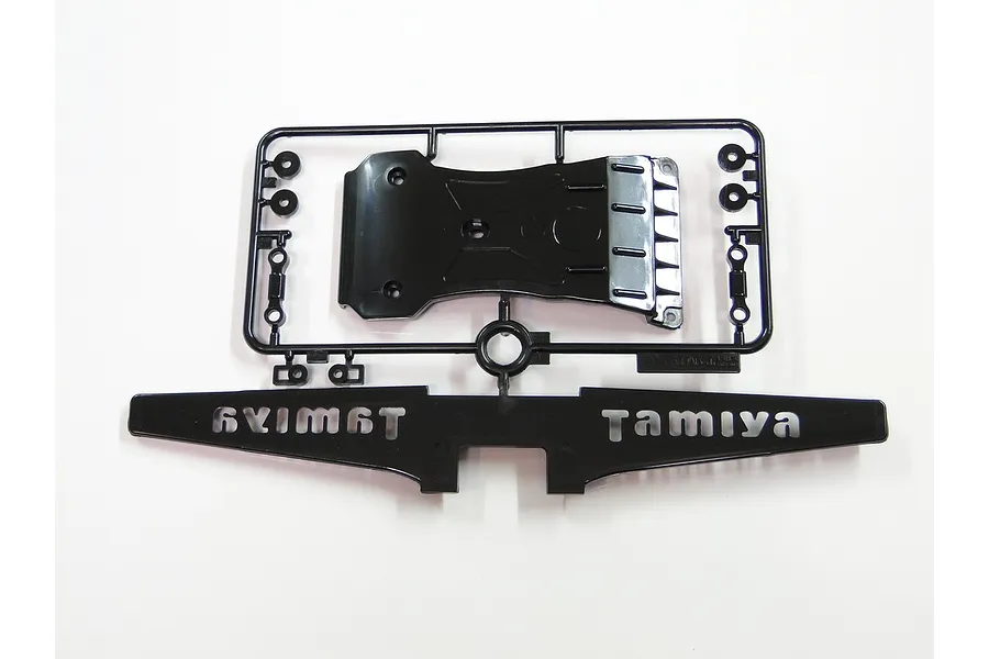 Tamiya black plastic parts tree showing a front bumper with raised lettering, a skid plate, and small washers on a white background.