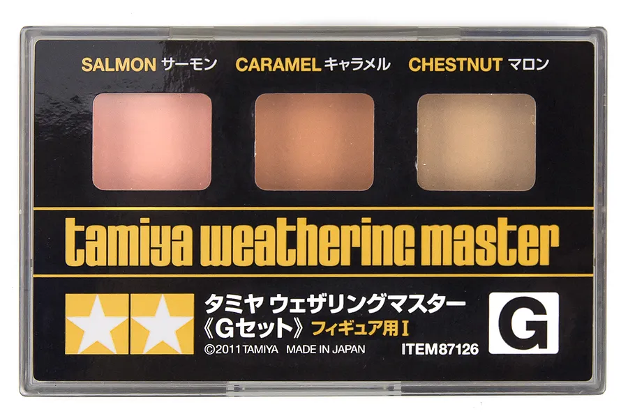 Tamiya Weathering Master Set G, featuring three pigment pans in Salmon, Caramel, and Chestnut, housed in a clear plastic case.