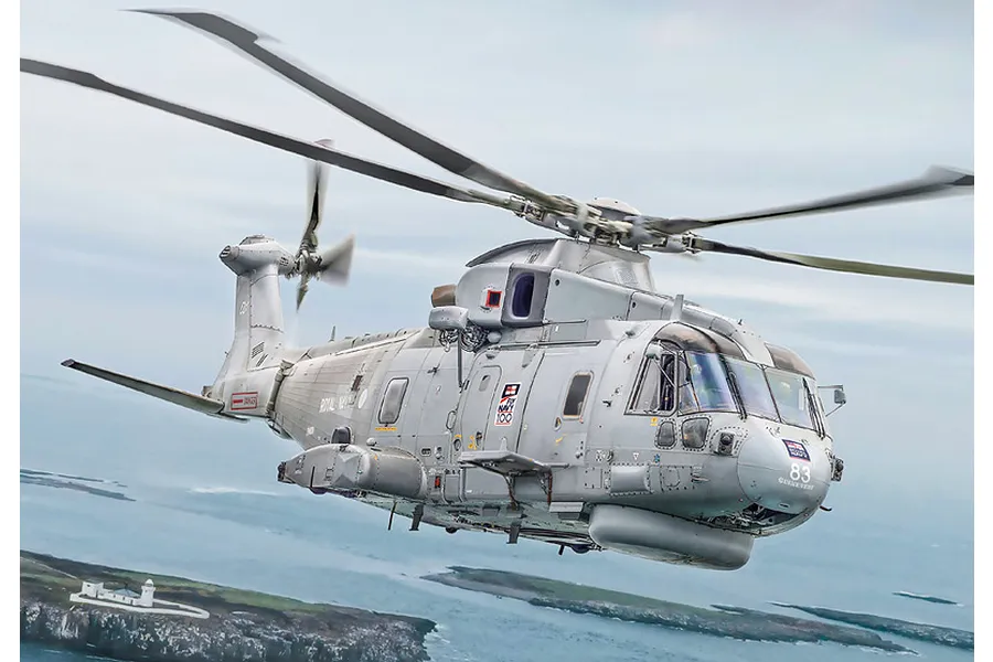 A grey Royal Navy AW-101 Merlin helicopter in flight over a coastal landscape.