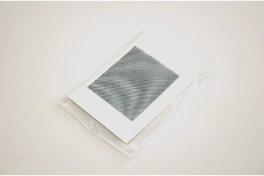 Photo-etched metal mesh sheet inside a protective plastic bag on a white surface.