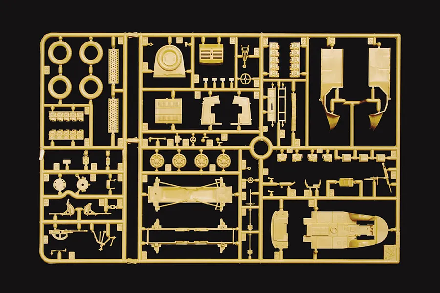 Tan plastic model kit sprue containing unassembled vehicle parts, wheels, and equipment against a black background.