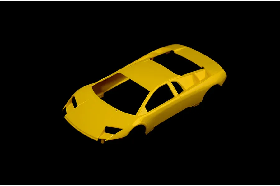 Unassembled yellow plastic model car body shell for a Lamborghini Murcielago against a black background.