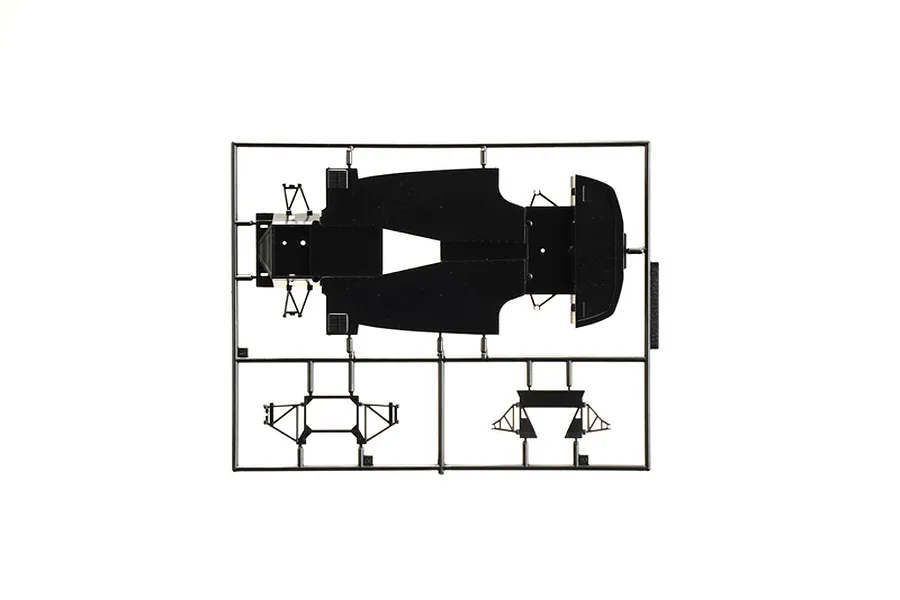 Black plastic model kit sprue containing a chassis pan and suspension parts on a white background.