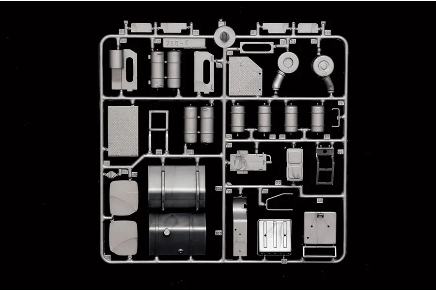 Grey plastic model kit sprue containing various truck parts such as fuel tanks, steps, and air filters against a black background.