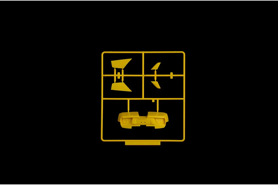 Yellow plastic model kit sprue containing car parts including a rear bumper and wing sections against a black background.