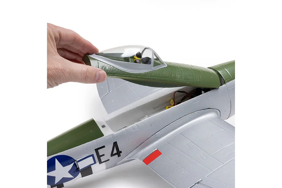 Human hand lifting the green and silver canopy hatch of the E-Flite micro P-47 Thunderbolt RC airplane against a white background.