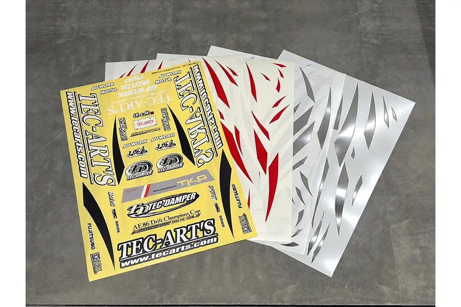 Multiple RC car decal sheets featuring TEC-ARTS branding, sponsor logos, and various decorative graphic stripes laid out on a dark surface.
