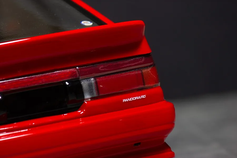 Close-up of the rear tail light and spoiler on a red RC model car body against a dark background.