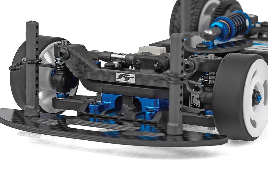 Close-up studio shot of the front suspension, carbon fiber shock tower, and blue aluminum parts on a Team Associated RC car.
