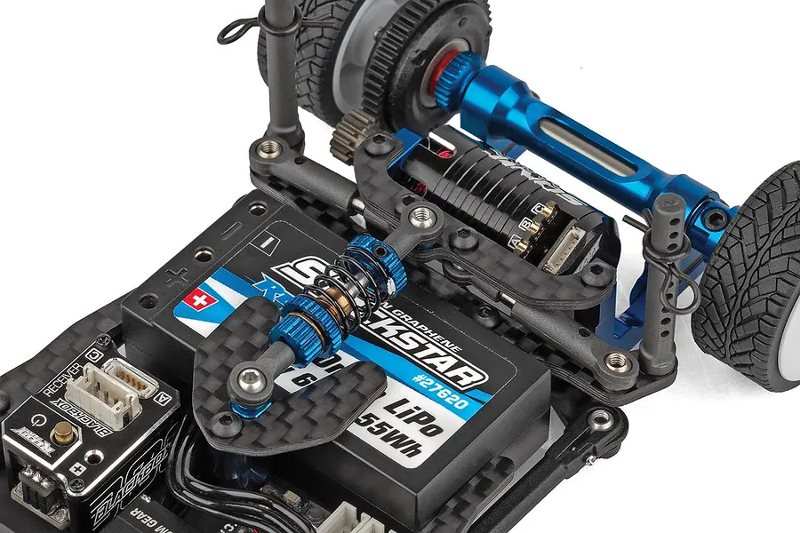 Close-up view of the internal chassis layout of a small scale RC car featuring a blue aluminium motor mount, carbon fiber shock tower, and installed electronic speed controller.