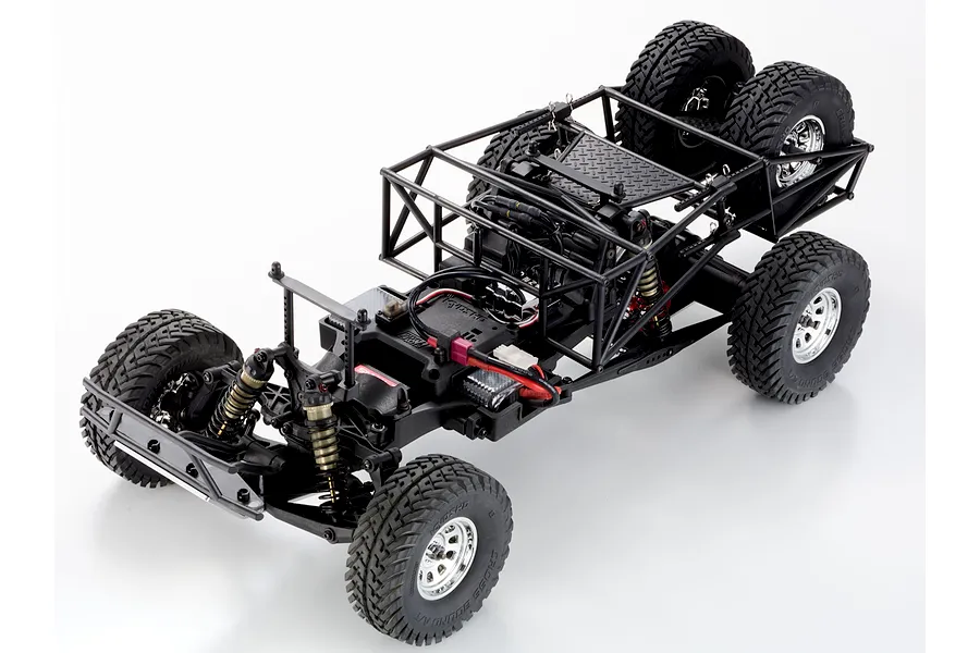 Top-down studio shot of the Kyosho Outlaw Renegade 2RSA RC truck chassis showing roll cage, dual rear spare tires, and suspension.